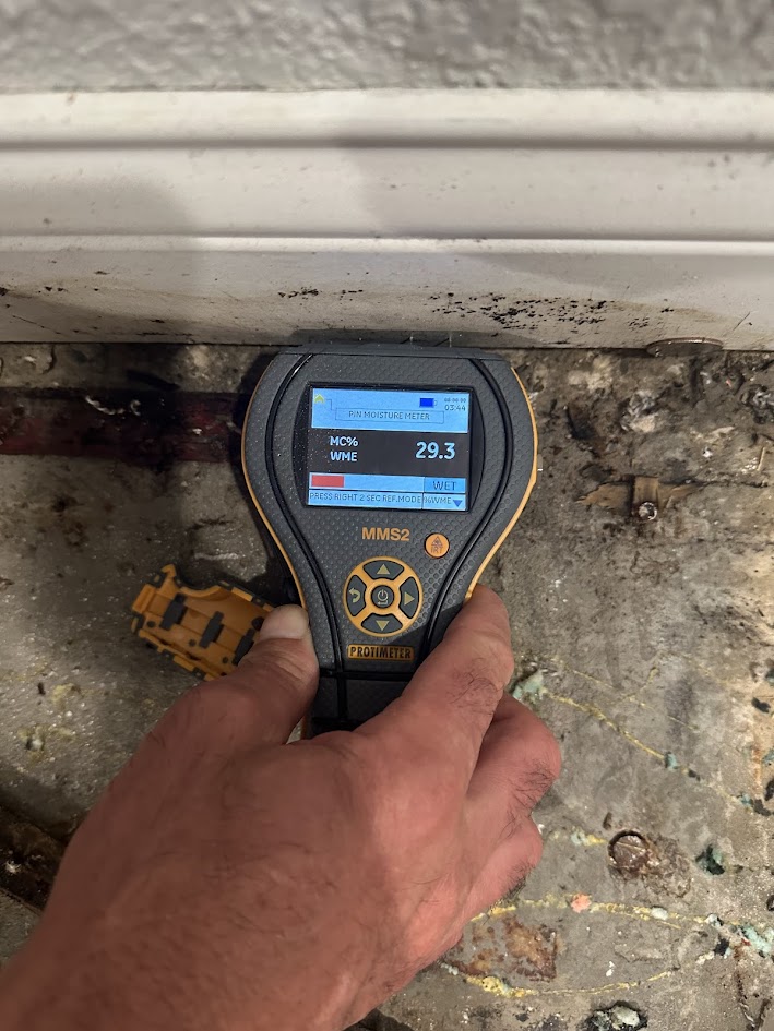 Binnacle technician taking a moisture reading at a water-damaged baseboard