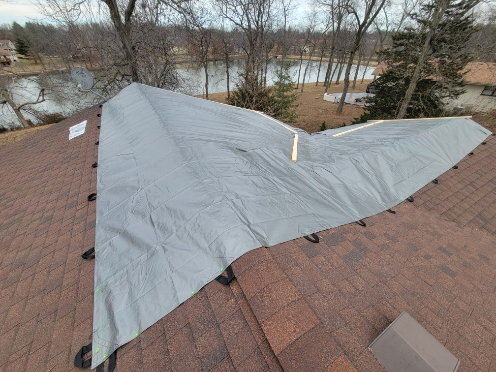 Lakefront home with emergency tarp installed over storm-damaged roof